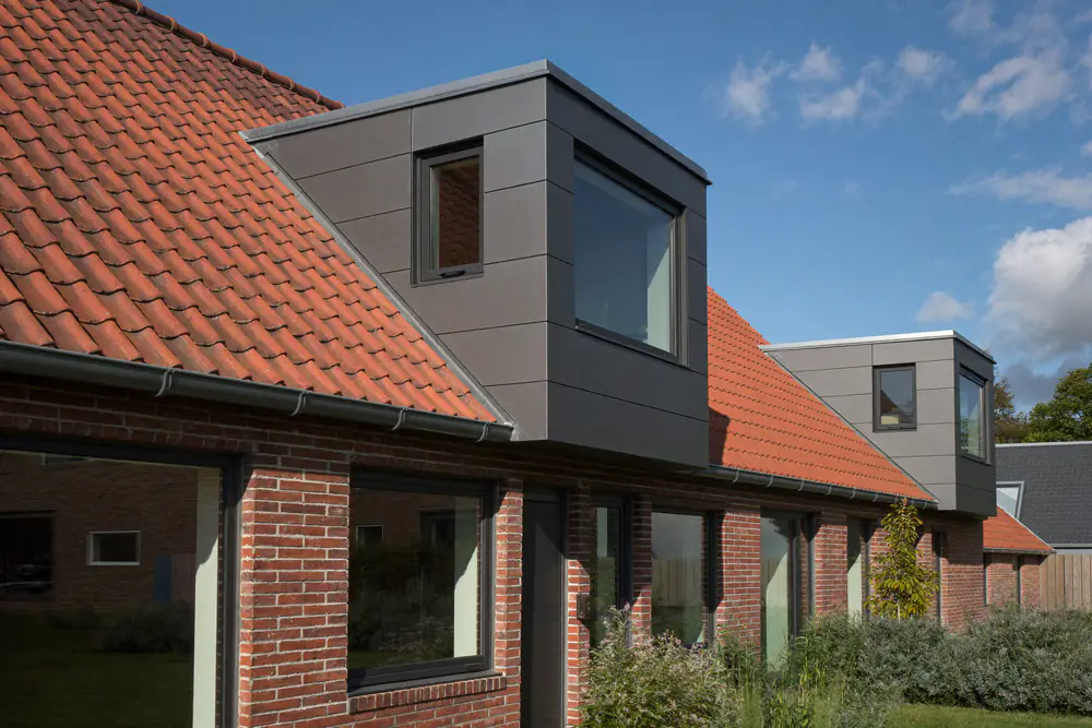 Dakkapel met antracietgrijze aluminium panelen en slanke zwarte kozijnen op een rood pannendak