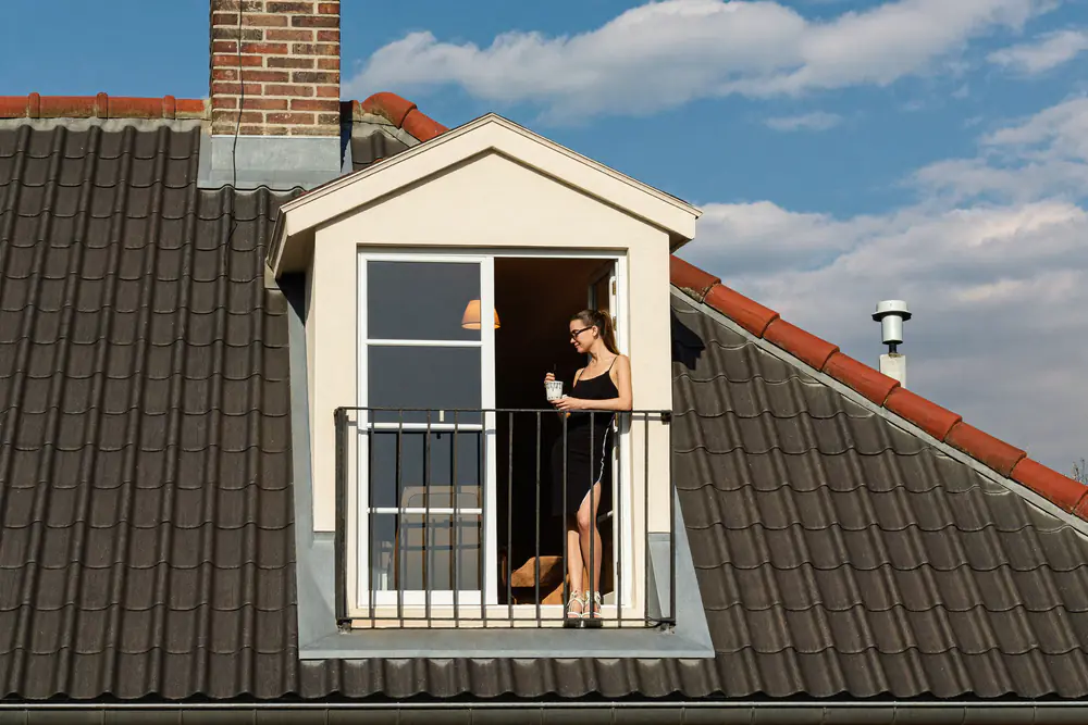 Dakkapel met openslaande glazen deuren en een Frans balkon, een vrouw staat in de deuropening