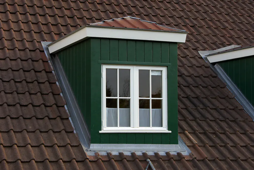 Groen geschilderde houten dakkapel met witte kozijnen op een pannendak