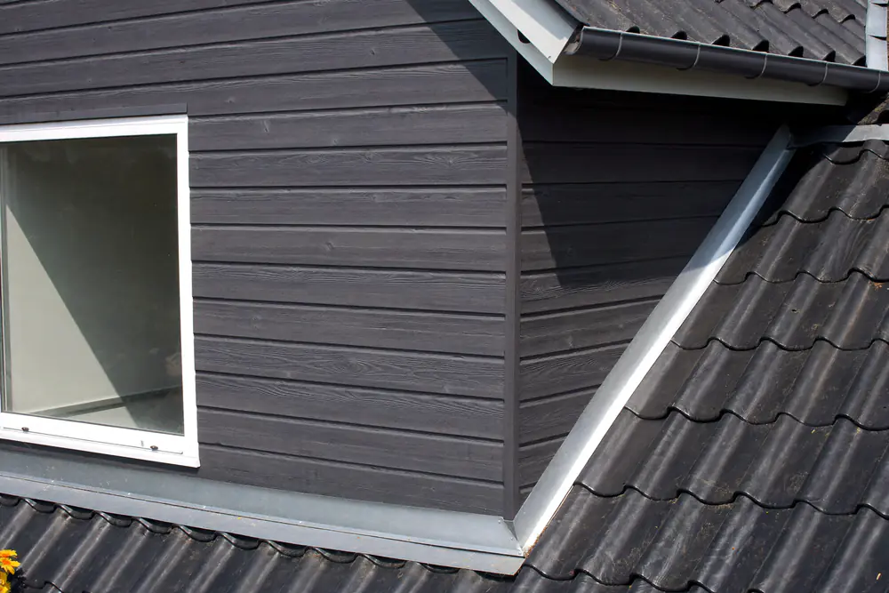 Donkergrijze horizontale bekleding op de zijwang van een dakkapel naast een wit kozijn