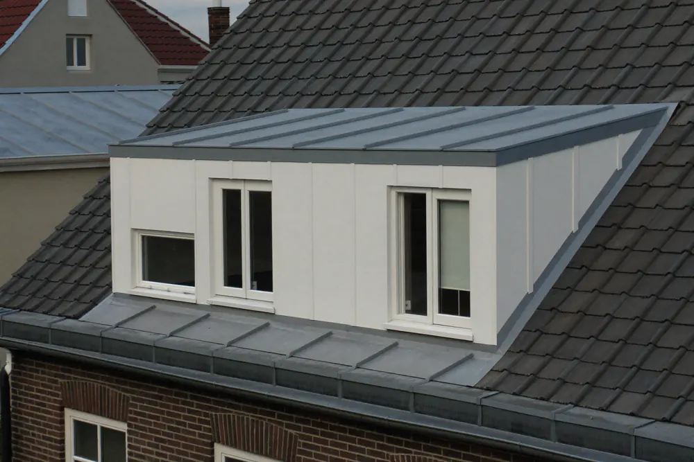 Witte kunststof dakkapel met een openstaand kiepraam naast rode dakpannen