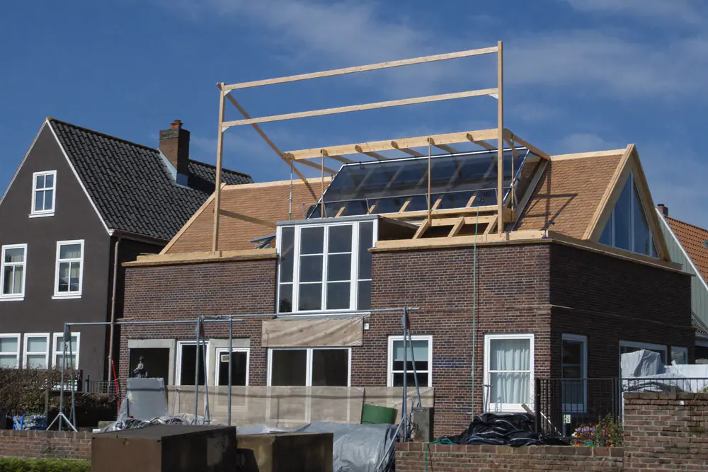 Bakstenen woning met een nieuw houten dakframe, de nok is omhooggebracht, steigers eromheen