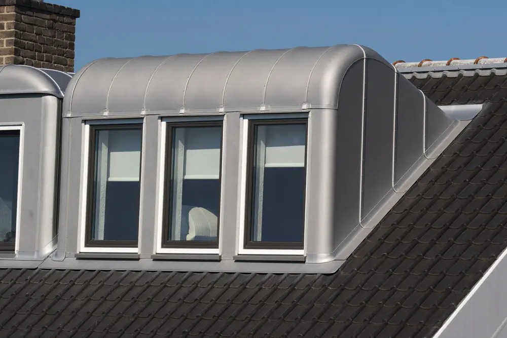 Zilvergrijze dakkapellen van polyester met afgeronde daken en witte kozijnen op een donker pannendak