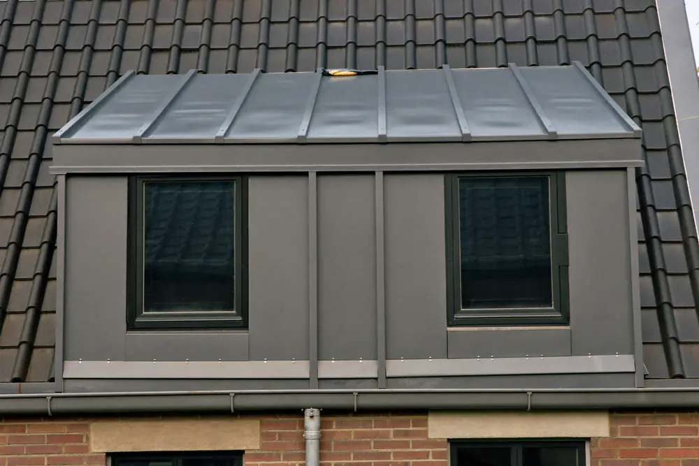 Dakkapel met mat grijze zinken bekleding en donkere kozijnen op een pannendak