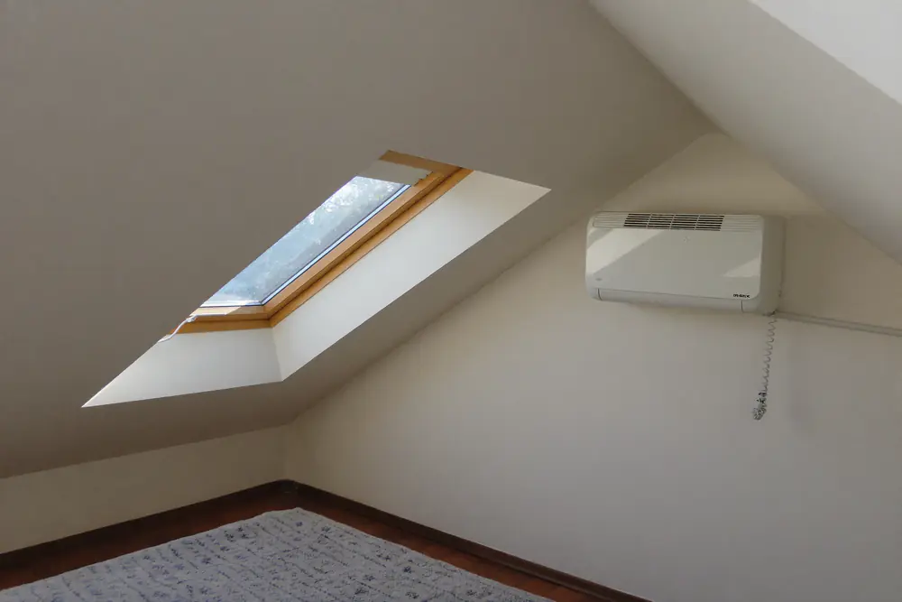 Zolderkamer met een witte airco aan de wand, een dakraam en een schuin plafond