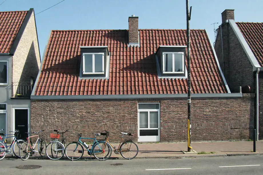 Bakstenen huis met een steil pannendak en twee dakkapellen met witte kozijnen, fietsen op straat