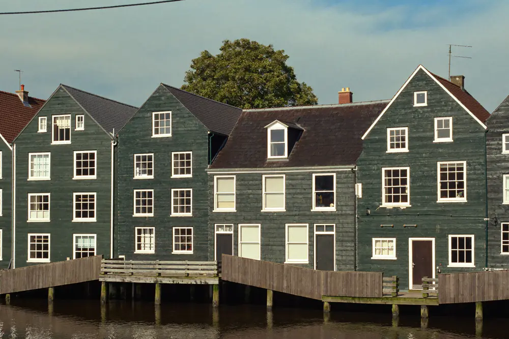 Rij donkergroene houten woningen in Zaanse stijl aan het water, met witte raamkozijnen
