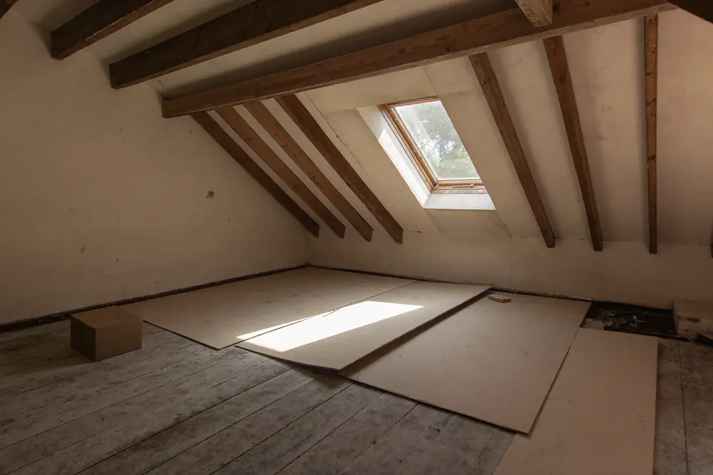 Lege zolder met houten spanten, een kale vloer en een dakraam waar het licht door valt